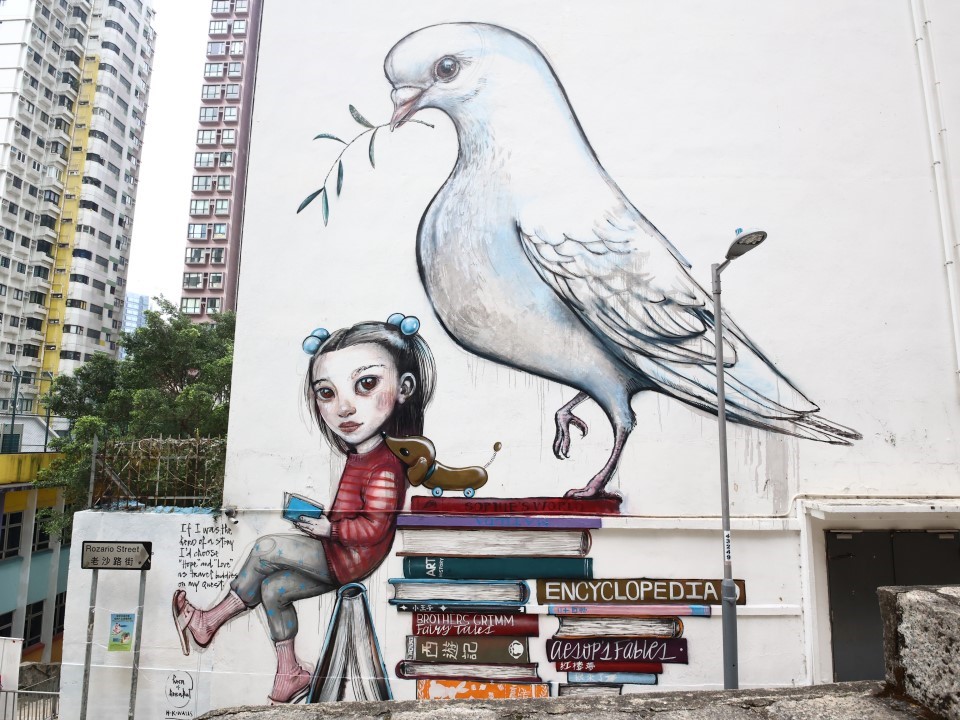 老沙路街上有Hera创作的大型壁画，画中有白鸟和女孩，周围是两叠书。 